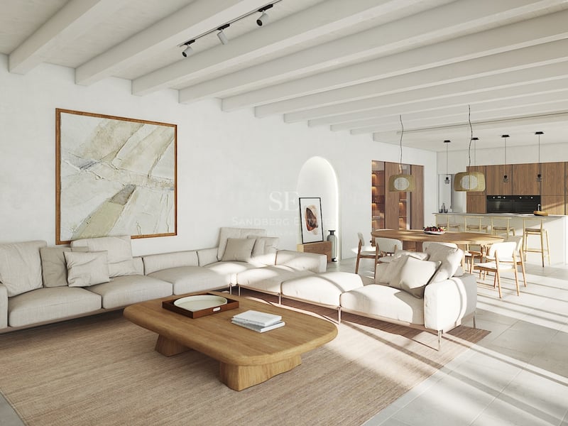 Salon lumineux à aire ouverte avec poutres blanches, canapé modulaire, table en bois et cuisine intégrée.