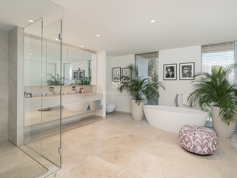 Modernes Badezimmer mit Travertinboden, Doppelwaschtisch, Glasdusche und einer weißen freistehenden Badewanne.