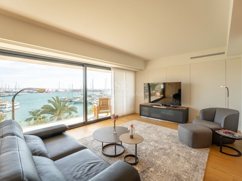 Modernt vardagsrum med svart lädersoffa och stora fönster med utsikt över en solig marina.