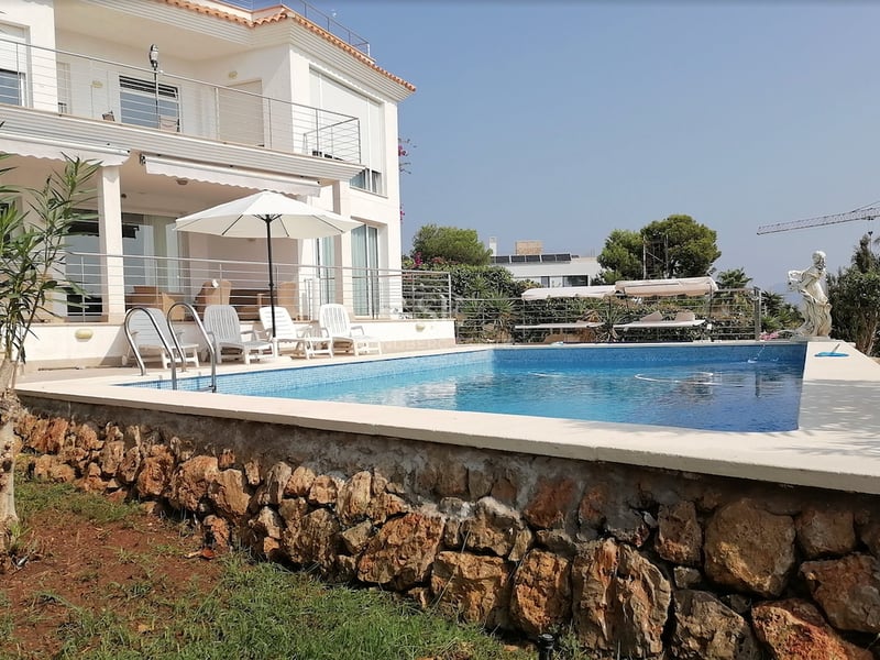 Piscine privée avec chaises longues devant une villa blanche aux murs en pierre naturelle.