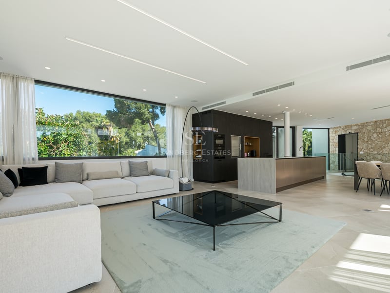 Salon et cuisine modernes à aire ouverte avec de grandes fenêtres donnant sur des arbres et un mur en pierre naturelle.