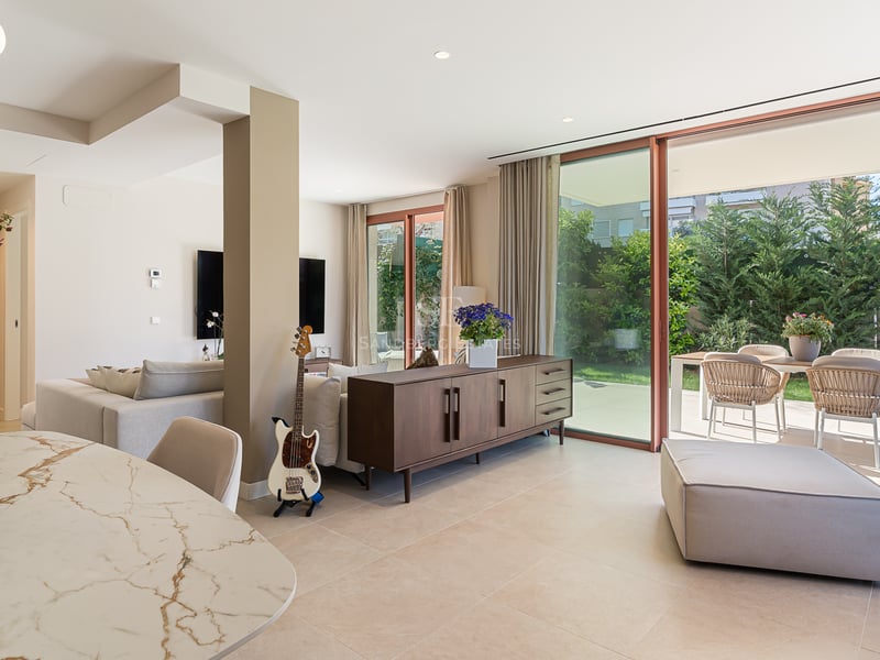 Modern living room with marble dining table, wood sideboard, and floor-to-ceiling glass doors opening to a garden.