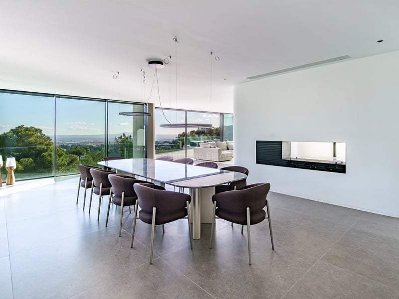 Salle à manger moderne élégante avec une grande table, des chaises sombres et des baies vitrées donnant sur la nature.