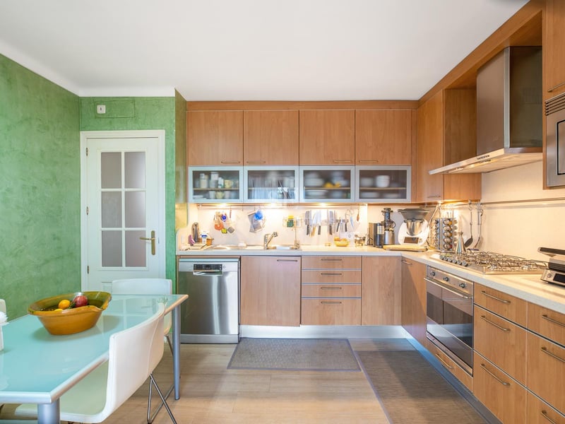 Moderne Holzküche mit Edelstahlgeräten, grüner Akzentwand und einem Glas-Esstisch.