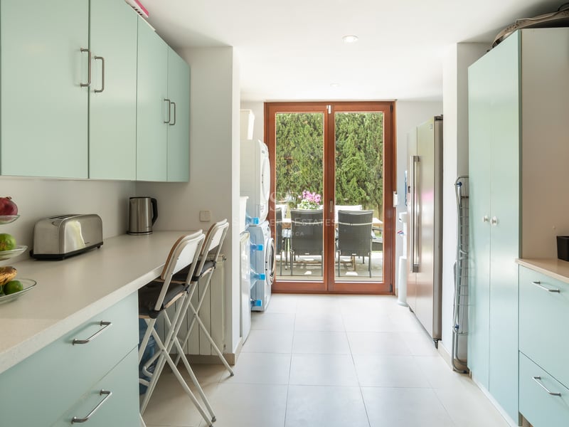 Cuisine lumineuse avec placards vert menthe, plans de travail blancs, coin buanderie et accès au patio verdoyant.