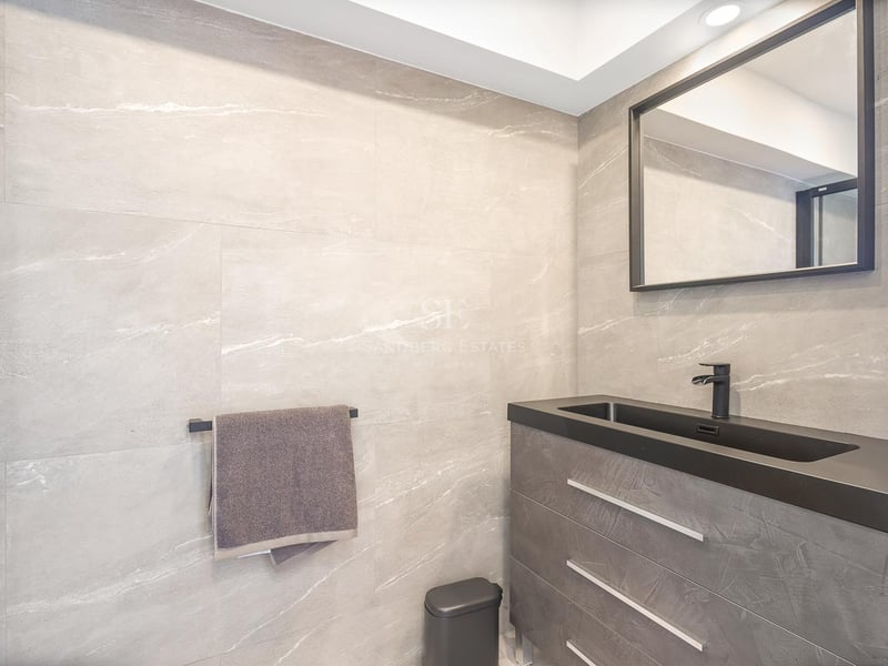 Moderner Waschtisch mit grauen Steinfliesen, schwarzem integriertem Waschbecken und schwarzem Spiegelrahmen.