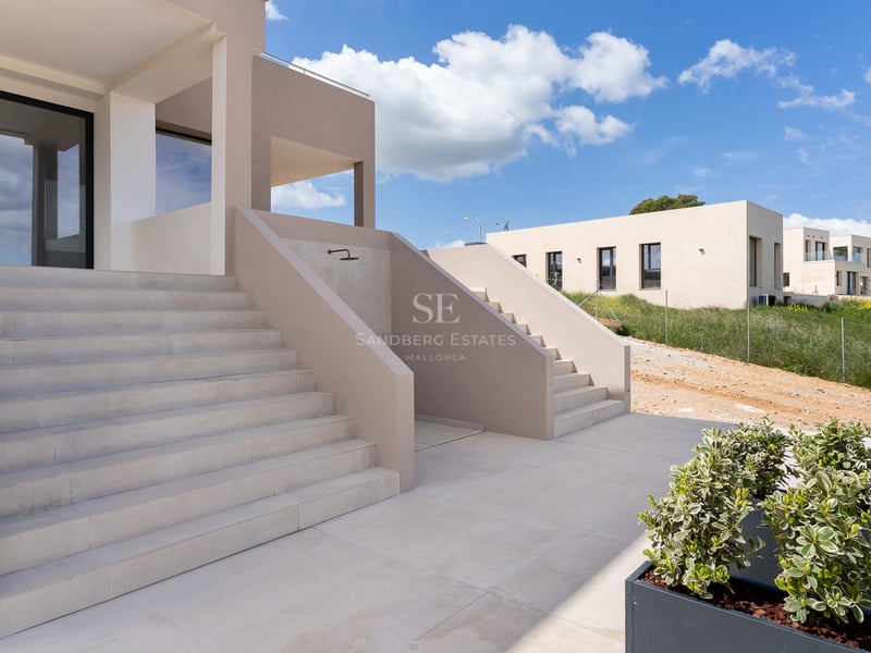 Moderne Natursteintreppen führen zu einer beigen Villa unter strahlend blauem Himmel.