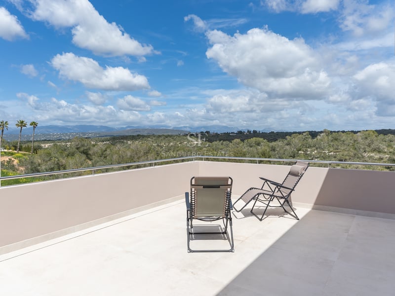 Minimalistische Dachterrasse mit zwei Sonnenliegen und weitem Blick über grüne Täler und ferne Berge.