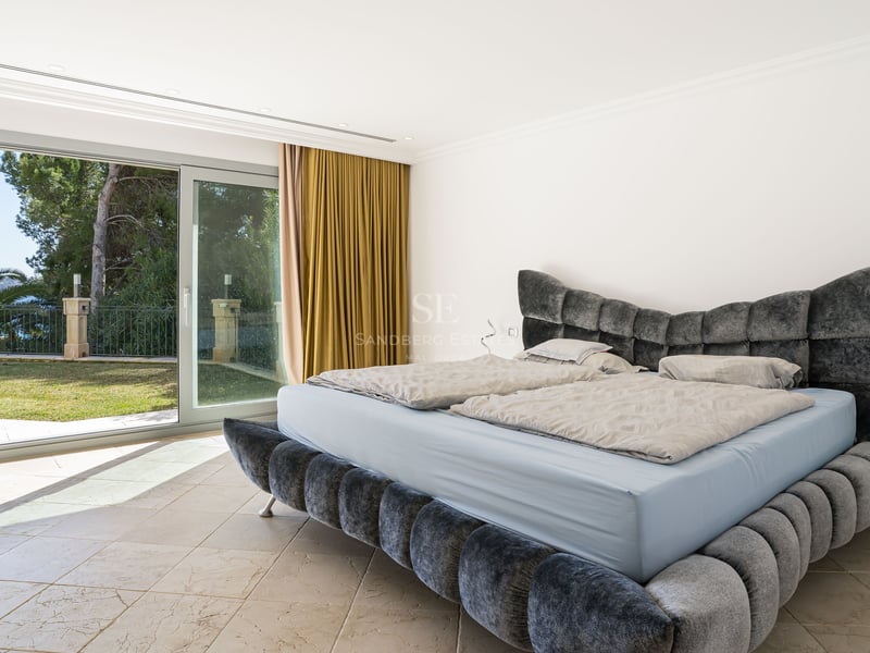 Zeitgenössisches Schlafzimmer mit grauem Samtbett und Glasschiebetüren zum mediterranen Garten.