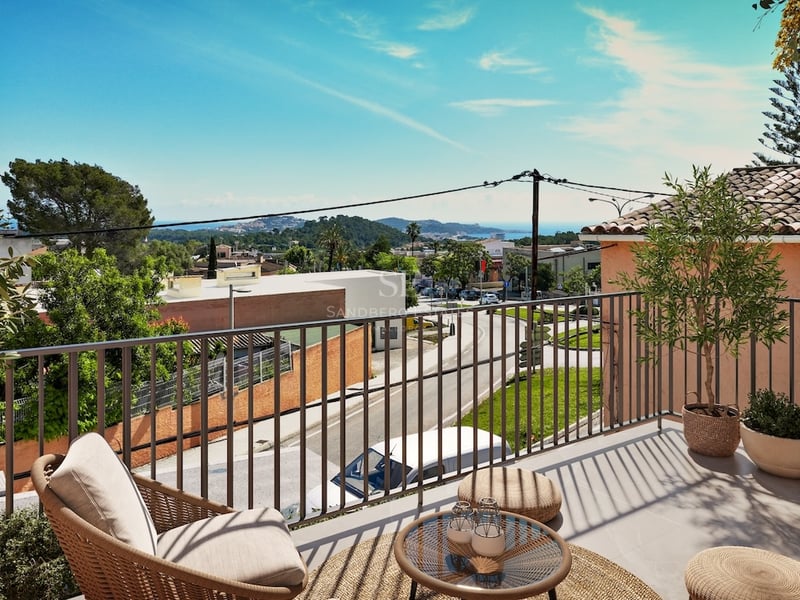 Sunlit terrace with wicker furniture overlooking a coastal town and the sea under a clear blue sky.