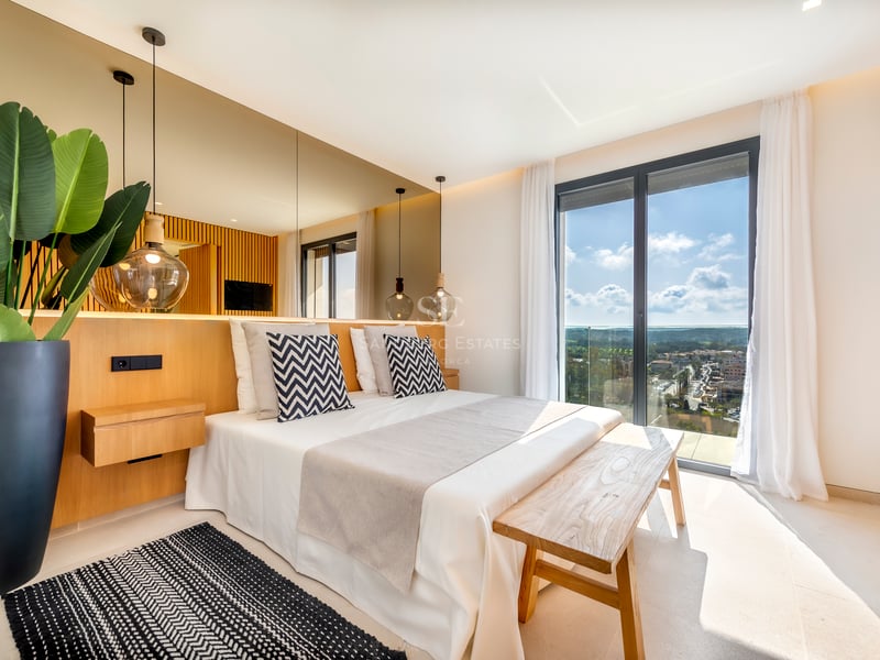 Chambre moderne avec finitions en chêne, baie vitrée toute hauteur et mur en miroir derrière le lit.