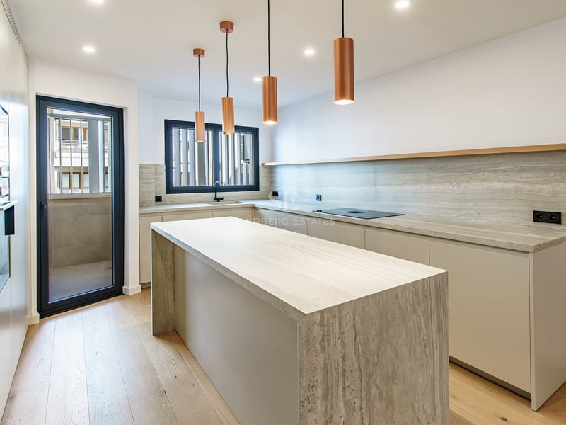 Cuisine lumineuse avec îlot en travertin, suspensions en cuivre et parquet en bois clair.