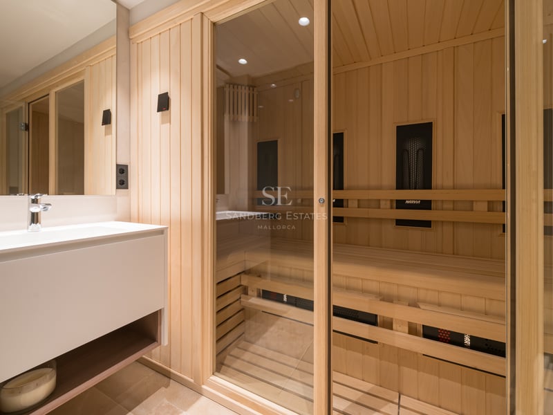 Sauna moderne en bois clair avec porte vitrée à côté d'un meuble vasque blanc minimaliste.