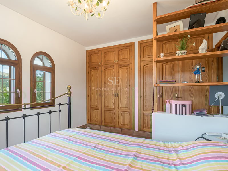 Bedroom featuring a wrought iron bed, large pine wardrobes, and arched windows with mountain views.