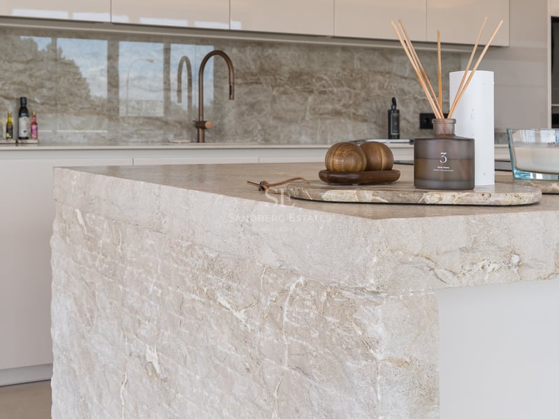 Nahaufnahme einer Kücheninsel aus Naturstein mit Kupfer-Armatur und minimalistischen Dekoelementen.