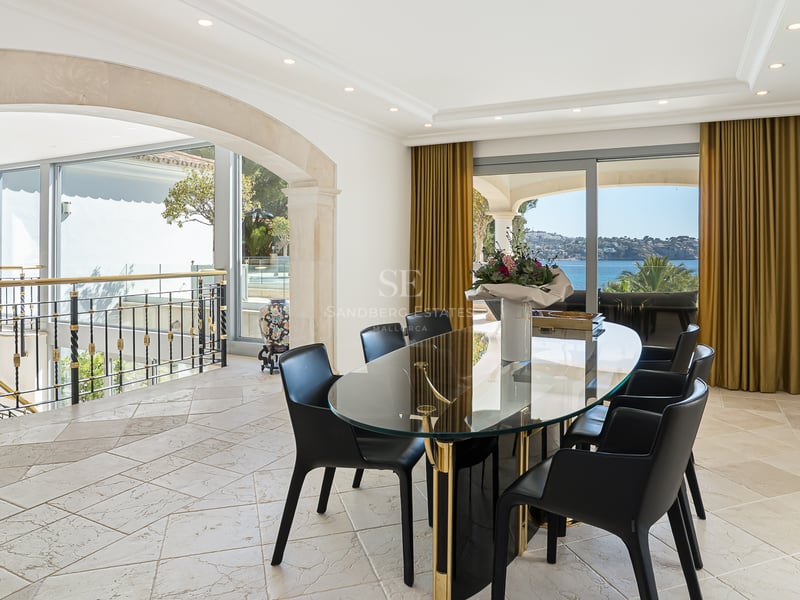 Moderner Essraum mit ovalem Glastisch, schwarzen Stühlen und großen Fenstern mit Blick auf das Mittelmeer.