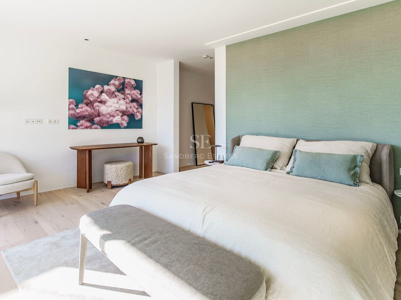 Chambre principale lumineuse avec mur vert sauge, grand lit et mobilier design sur parquet clair.