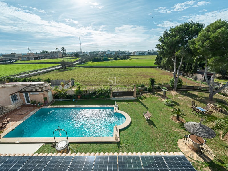 Vue d'en haut d'une piscine turquoise, jardin verdoyant et panneaux solaires surplombant la campagne méditerranéenne.