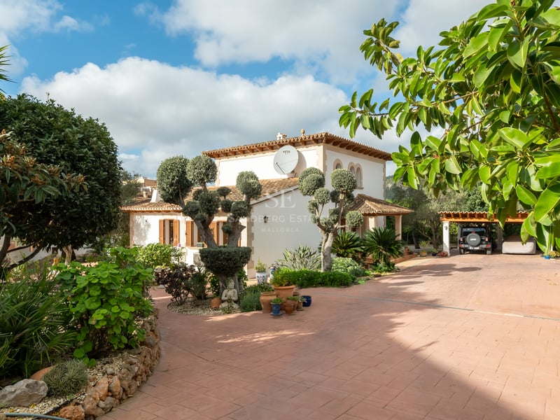 A sun-drenched Mediterranean villa with a terracotta driveway, manicured trees, and a covered carport.