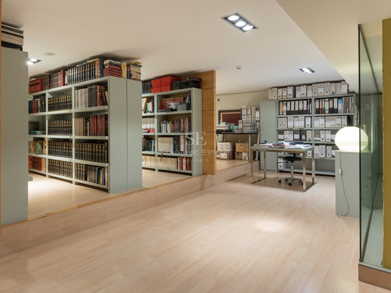 Grand bureau à domicile avec vastes rayonnages, parquet clair et bureau moderne en verre.
