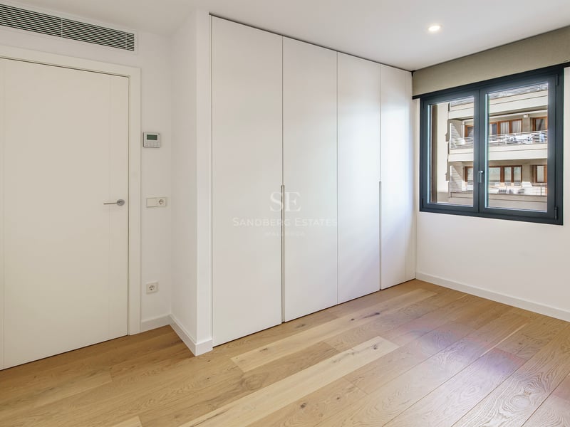 Chambre lumineuse avec parquet en bois clair, grands placards blancs intégrés et fenêtre au cadre sombre.