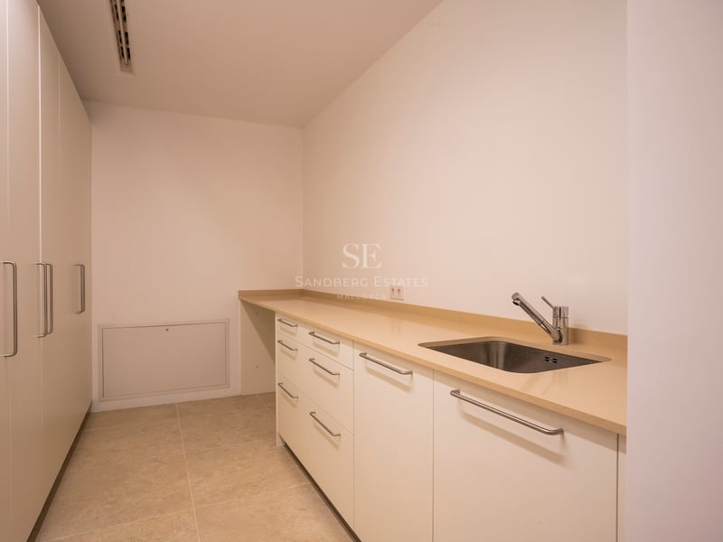 Weißer Wirtschaftsraum mit beiger Arbeitsplatte, Edelstahlspüle und deckenhohen Einbauschränken.