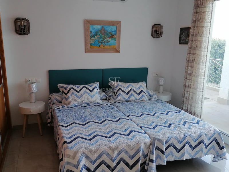 Chambre avec lits jumeaux, tête de lit bleu canard et grande baie vitrée ouvrant sur une terrasse ensoleillée.