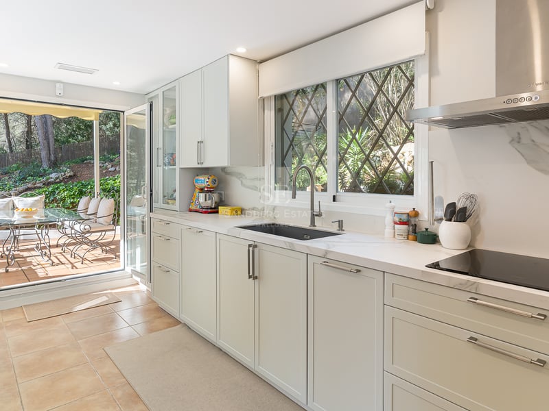 Bright kitchen with white cabinetry, marble countertops, and large glass doors opening to a lush garden terrace.