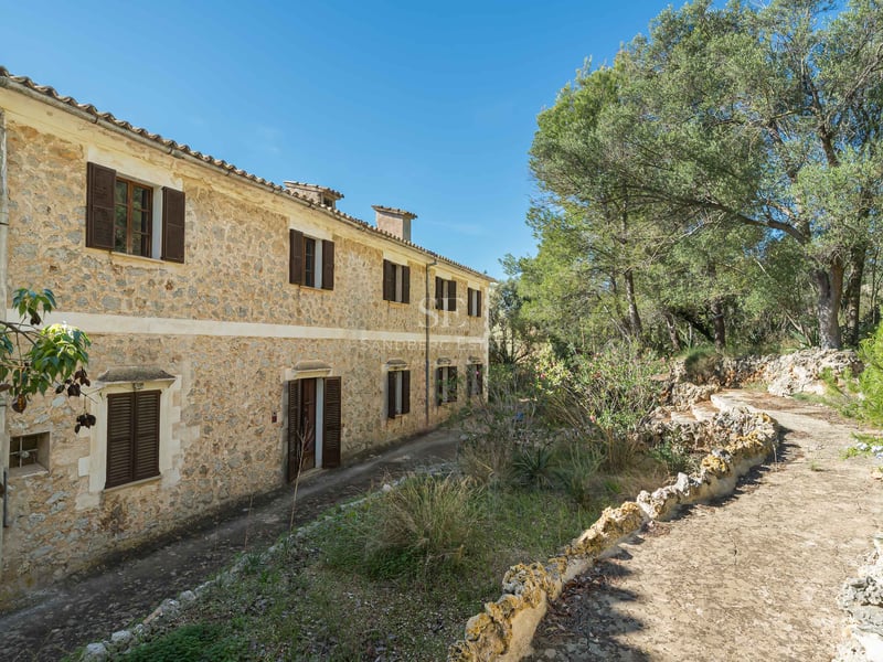 Un bâtiment rustique en pierre de deux étages avec des volets marron foncé entouré d'arbres verdoyants.