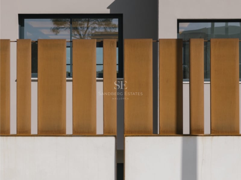 Weiße Begrenzungsmauer mit vertikalen Lamellen aus Cortenstahl und minimalistischer Fassade im Hintergrund.