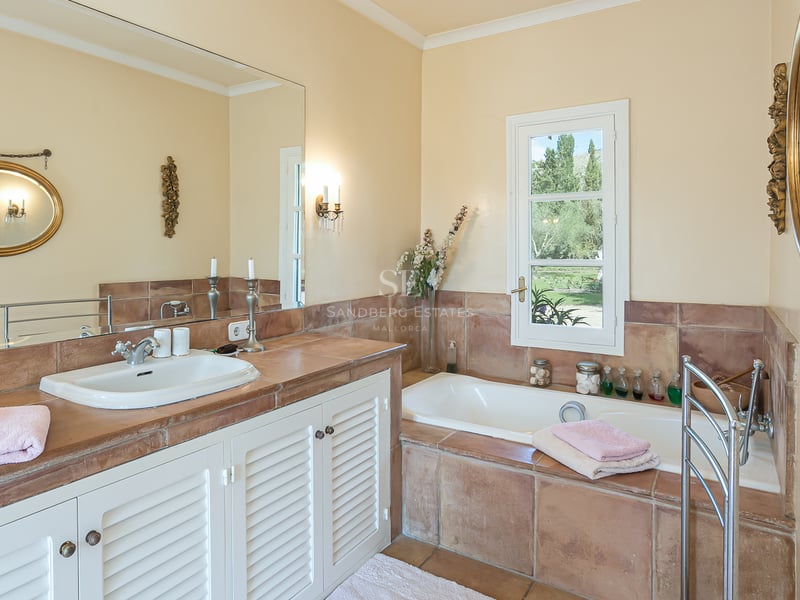 Salle de bain lumineuse avec plans en terre cuite, meubles à persiennes blanches, baignoire encastrée et miroirs.