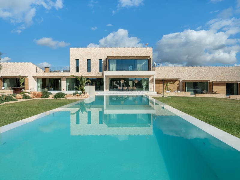 Modern tvåvåningsvilla med en stor rektangulär pool och naturstensfasad under en blå himmel.