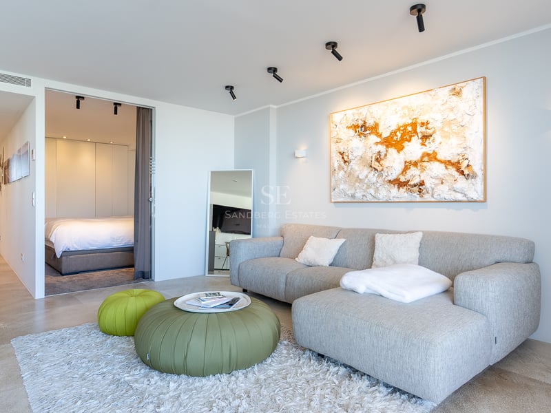 Helles Wohnzimmer mit grauem Sofa, grünen Hockern und Blick in das angrenzende Schlafzimmer.