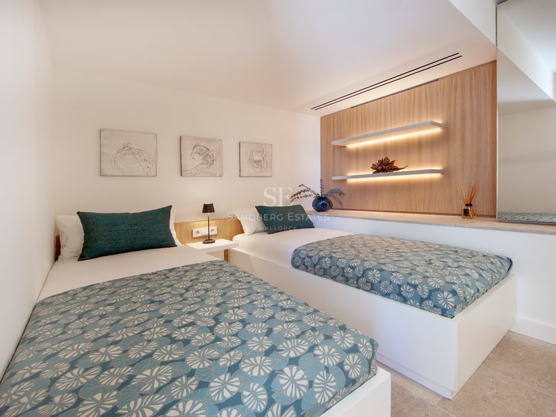 Chambre moderne avec deux lits simples, édredons à motifs bleu canard et étagères flottantes avec éclairage LED.