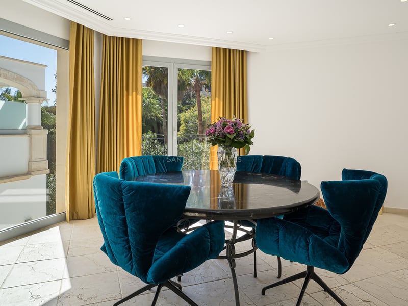 Moderner Essbereich mit rundem Marmortisch, blauen Samtstühlen und Blick durch bodentiefe Fenster.