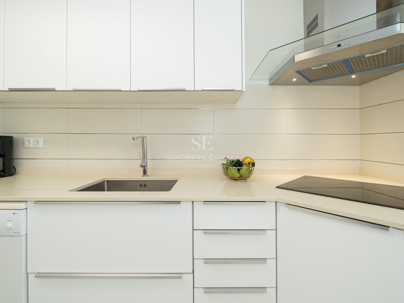 Close-up of a modern white kitchen featuring a stainless steel sink, glass hood, and ceramic cooktop.