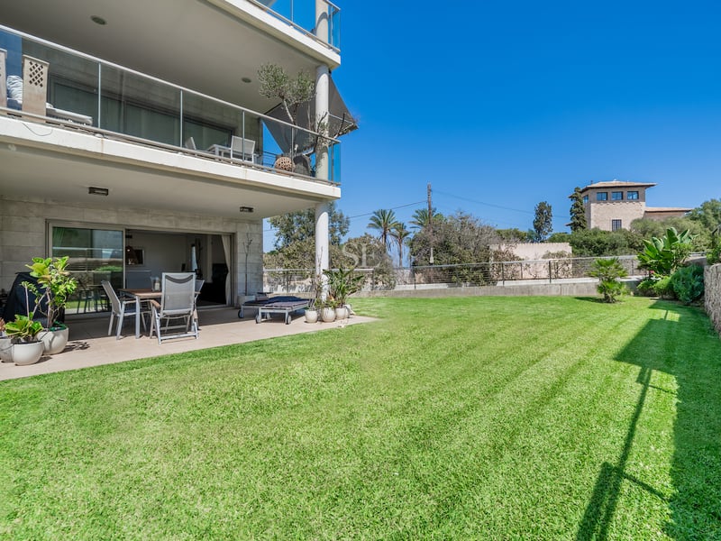Terrasse couverte avec mobilier d'extérieur ouvrant sur un grand jardin privé gazonné sous un ciel bleu.
