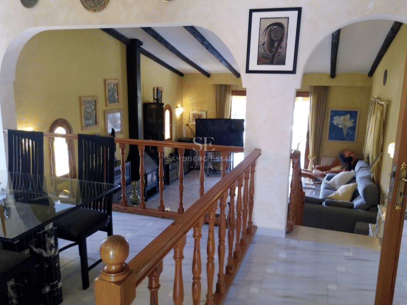 Interiör i två nivåer som visar en matplats med utsikt över ett nedsänkt vardagsrum med gula väggar och takbjälkar.