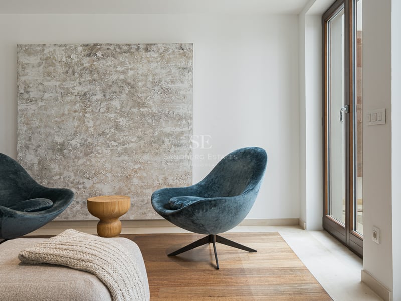 Deux fauteuils en velours bleu canard face à une grande toile abstraite à côté d'une baie vitrée toute hauteur.