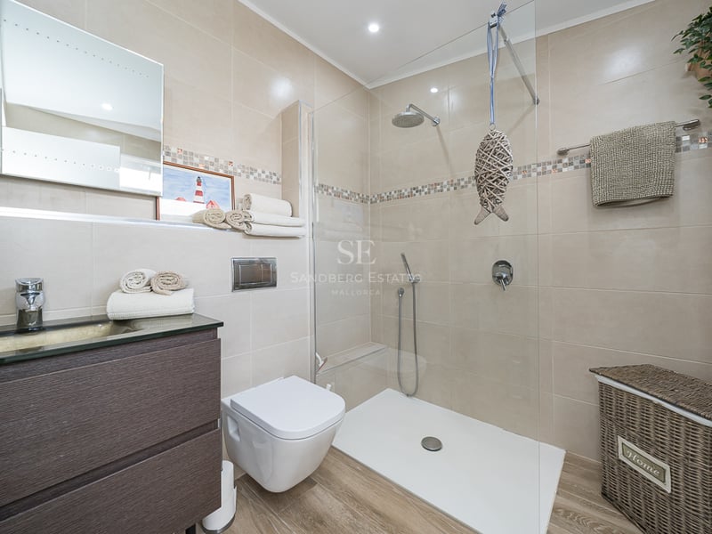Salle de bains contemporaine avec douche vitrée, meuble vasque en bois sombre et carrelage beige.
