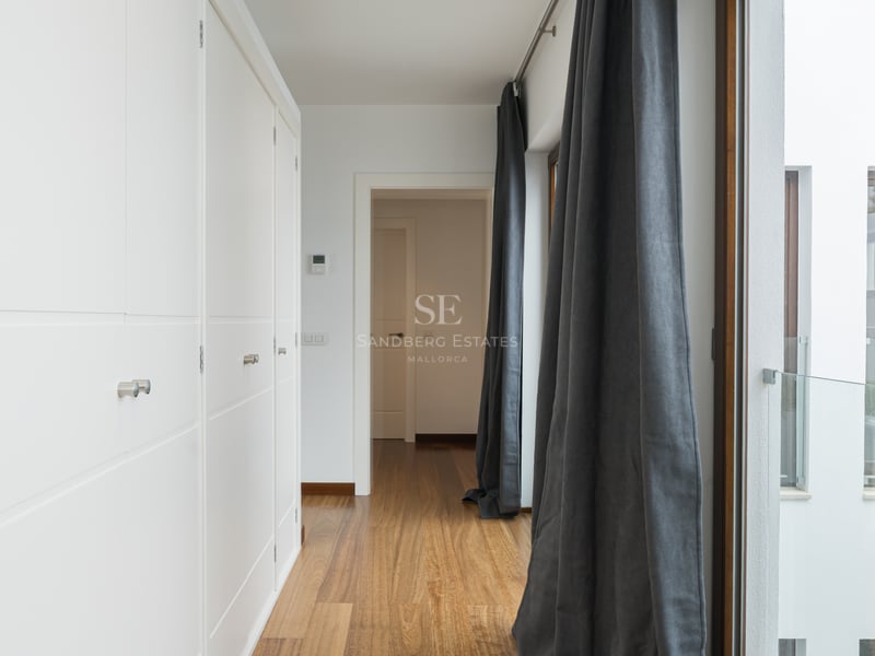 Couloir lumineux avec de grands placards blancs intégrés, parquet en bois chaleureux et rideaux gris anthracite.