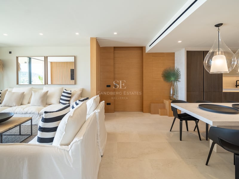 Salon moderne à aire ouverte avec canapés blancs, accents en chêne et salle à manger avec suspensions en verre design.