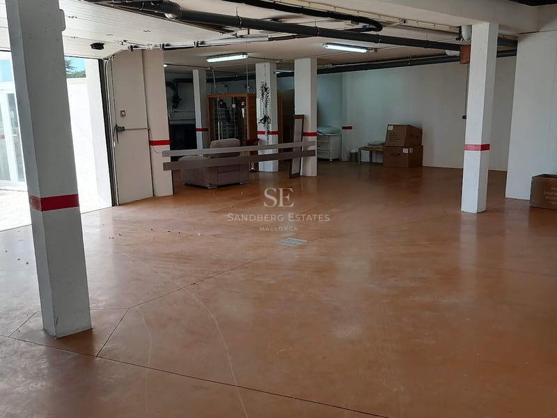 Vue intérieure d'un grand garage souterrain avec sol en époxy terre cuite, piliers blancs et tuyauterie apparente.