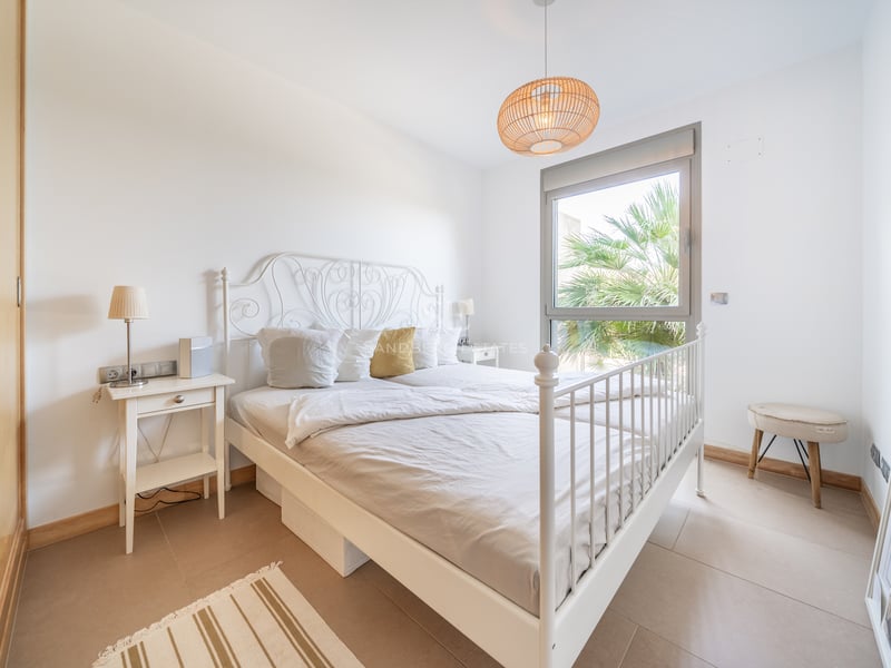Chambre avec lit en fer blanc, armoire intégrée en bois et fenêtre donnant sur un palmier.