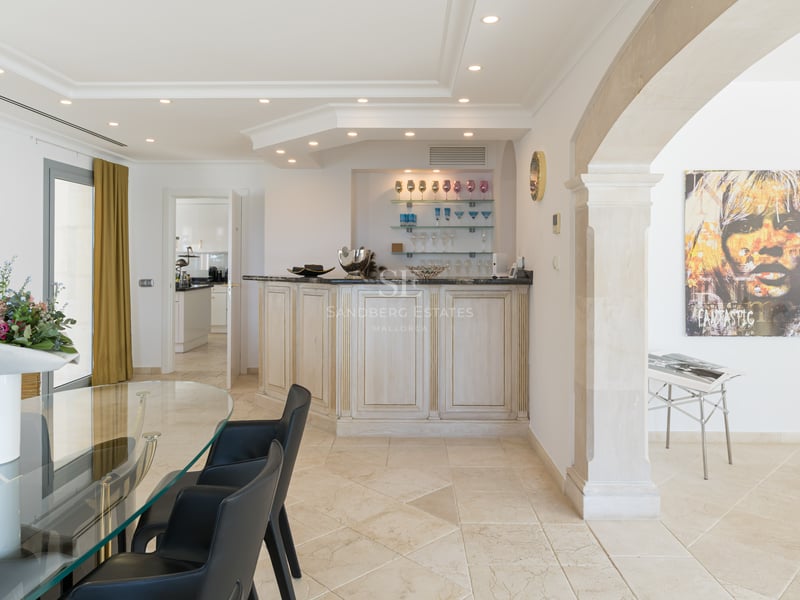 Modernes Esszimmer mit Glastisch, dunklen Stühlen, weißer Bar und klassischem Steinbogen.