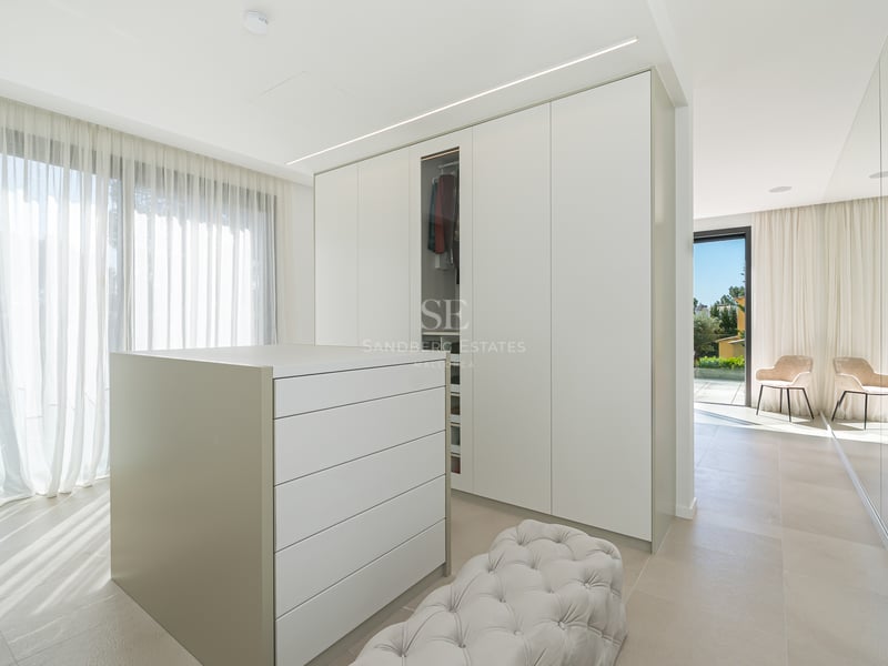 Dressing spacieux avec placards blancs, îlot central, pouf capitonné et vue sur mer par les grandes baies vitrées.