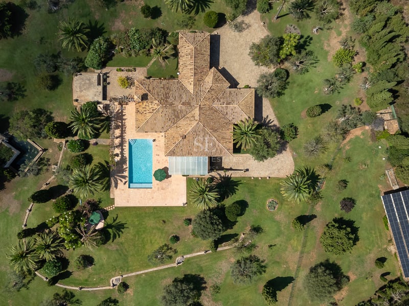 Vue aérienne d'une grande villa méditerranéenne avec piscine, jardins paysagers et panneaux solaires.