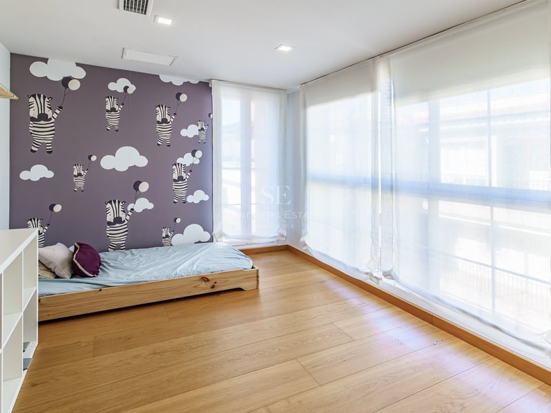 Ljust barnrum med zebramönstrad tapet, ljust trägolv och stora fönster med vita tunna gardiner.