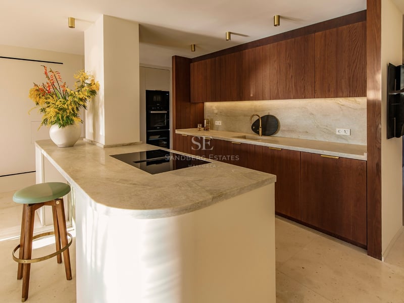 Moderne Küche mit dunklen Holzschränken, Naturstein-Arbeitsplatten und einer geschwungenen Insel mit Barhocker.