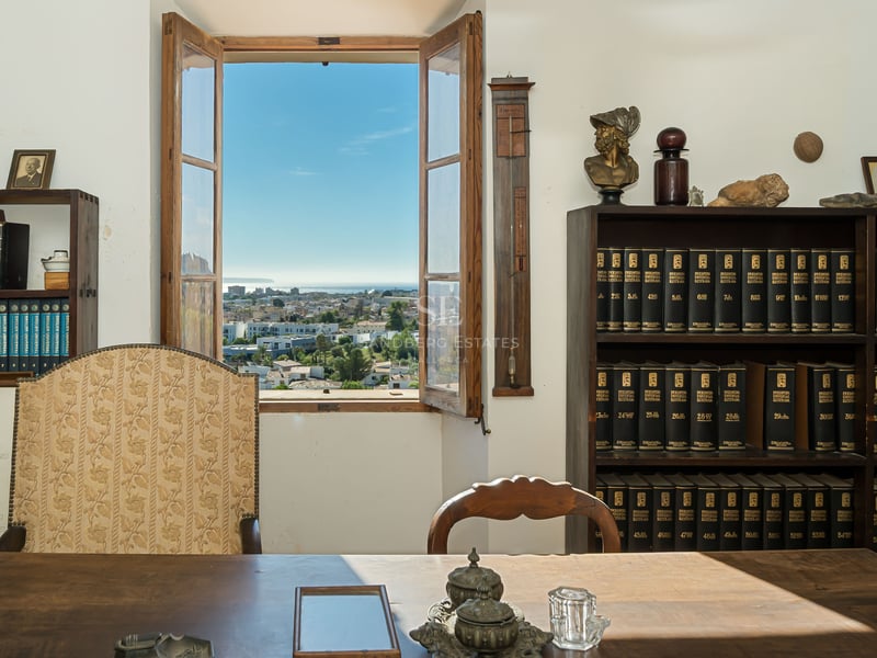 Bureau traditionnel en bois avec bibliothèques et fenêtre ouverte donnant sur la mer et la ville.